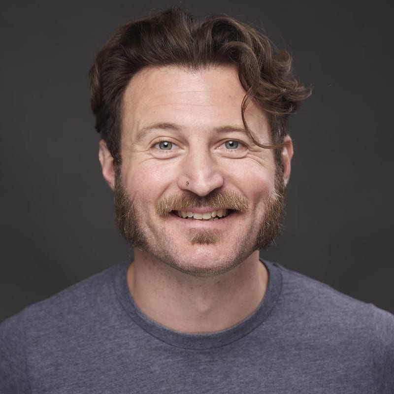 Will Soprano, smiling, in a gray T-shirt against a dark gray background.